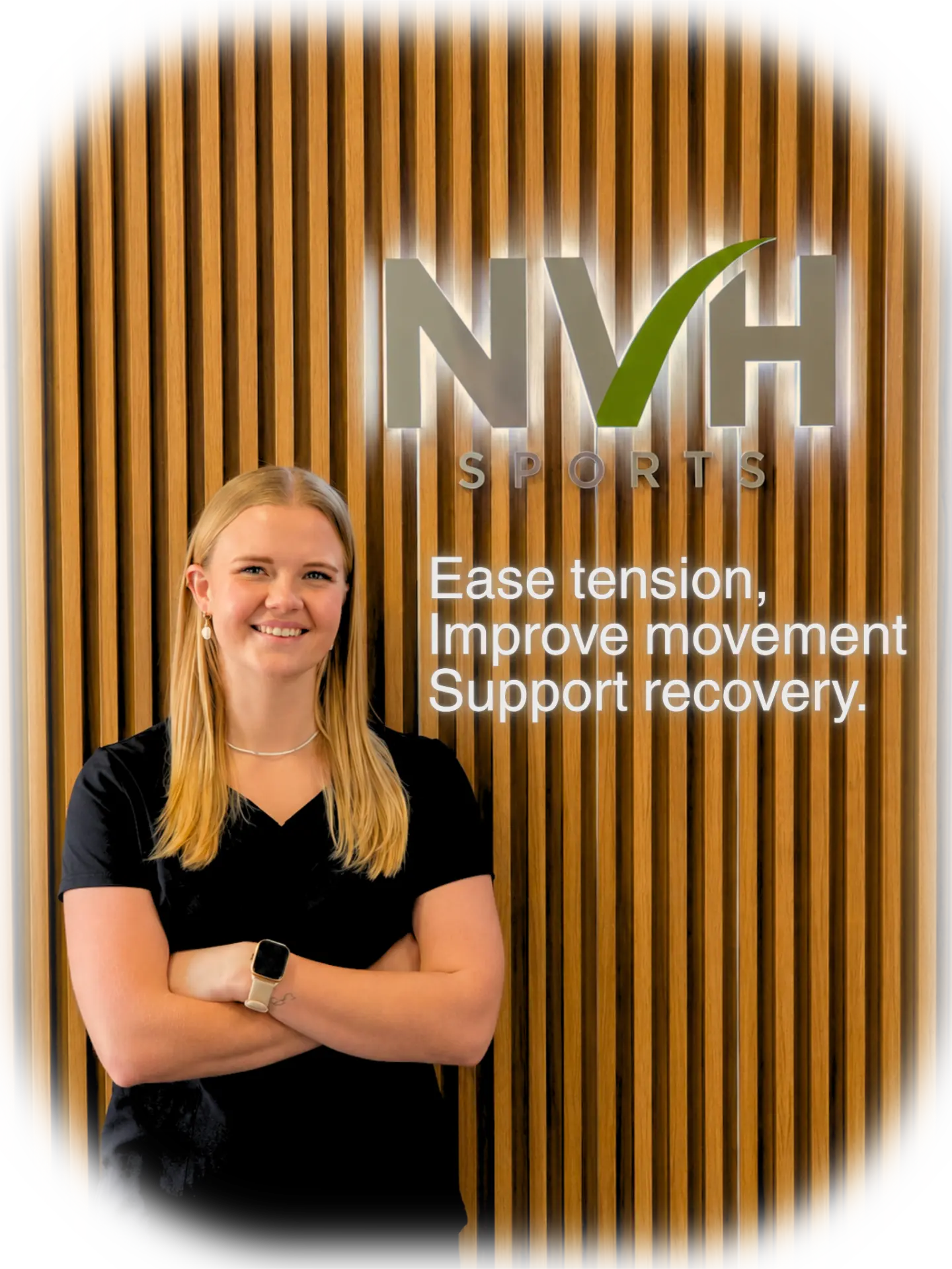Nadya, remedial sports massage therapist, in front of the NVH Sports illuminated logo. Ease tension, improve movement, support recovery.